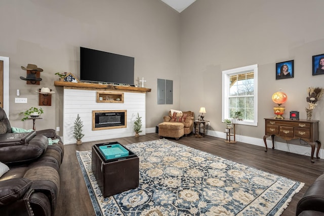 living area with a glass covered fireplace, wood finished floors, baseboards, and a towering ceiling