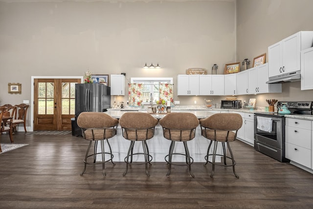 kitchen featuring a kitchen island, under cabinet range hood, a breakfast bar, a high ceiling, and electric range