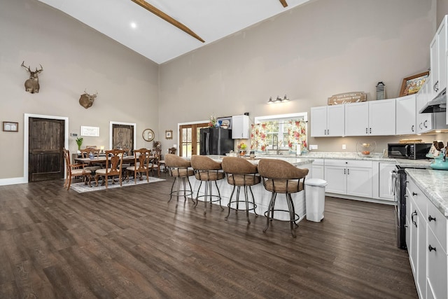 kitchen with dark wood-style floors, high vaulted ceiling, black appliances, and a kitchen bar