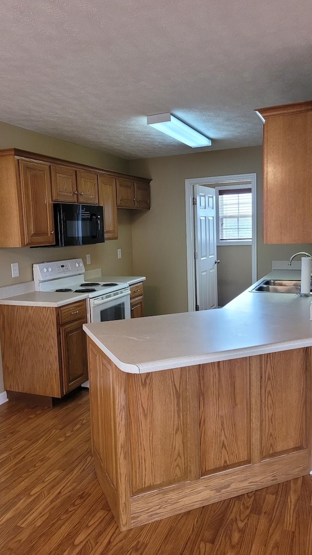 kitchen featuring a sink, white electric range, wood finished floors, a peninsula, and black microwave