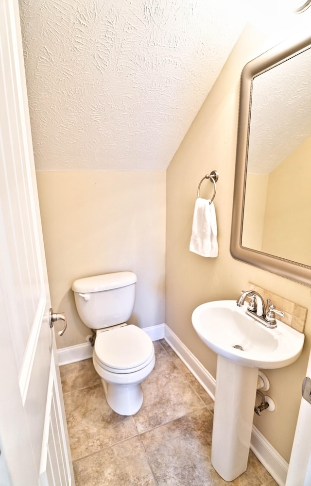 bathroom featuring baseboards, toilet, lofted ceiling, tile patterned floors, and a textured ceiling