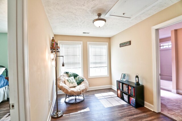 sitting room with wood finished floors, visible vents, baseboards, attic access, and a textured ceiling