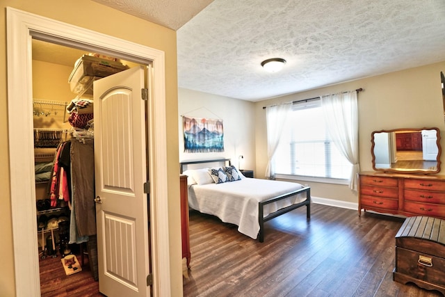 bedroom featuring dark wood-style floors, baseboards, a spacious closet, a closet, and a textured ceiling