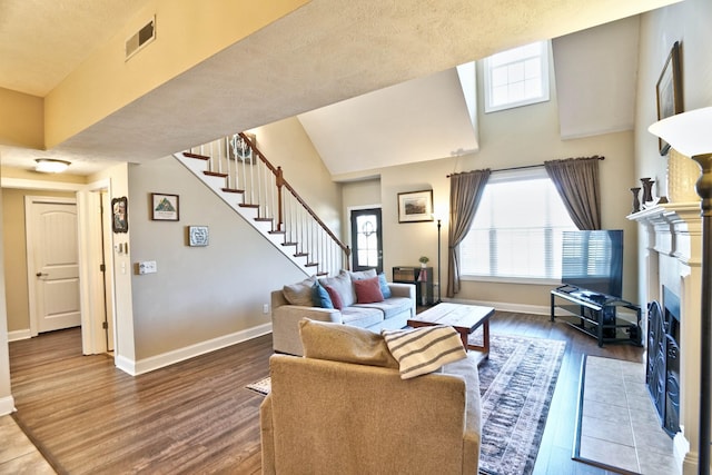 living room featuring baseboards, a fireplace with flush hearth, wood finished floors, and stairs