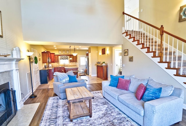 living area with dark wood-type flooring, a fireplace, baseboards, a towering ceiling, and stairs