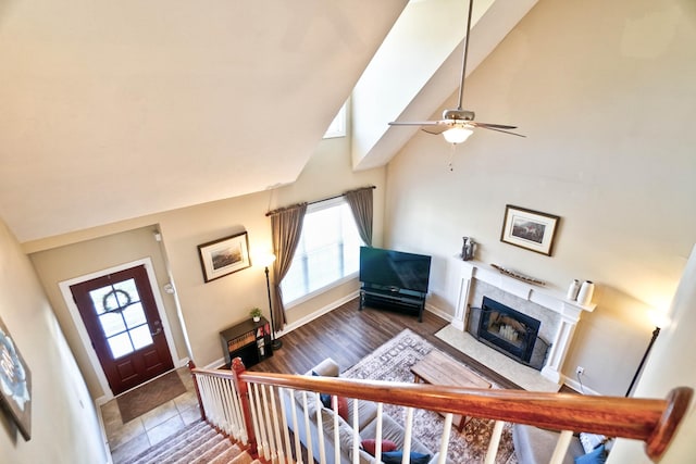 foyer entrance featuring a ceiling fan, wood finished floors, baseboards, high vaulted ceiling, and a premium fireplace