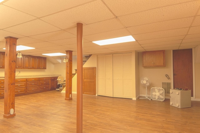 finished below grade area with visible vents, baseboards, light wood-type flooring, and a paneled ceiling