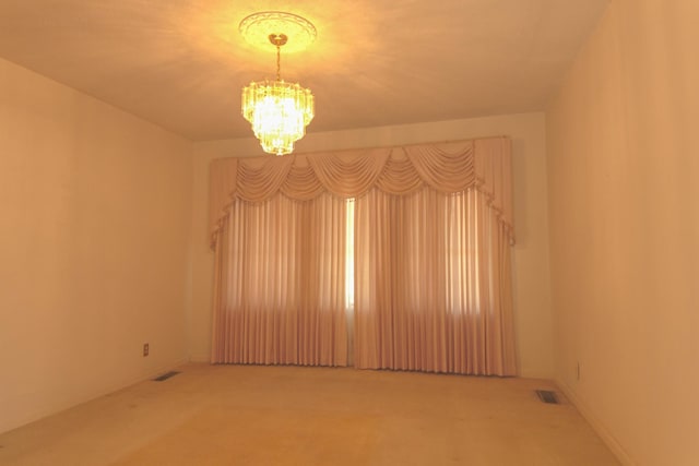 empty room featuring a notable chandelier, carpet flooring, and visible vents