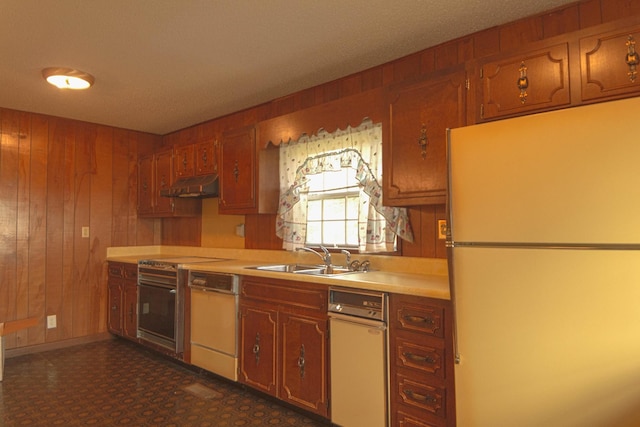 kitchen featuring under cabinet range hood, a sink, freestanding refrigerator, wood walls, and dishwashing machine