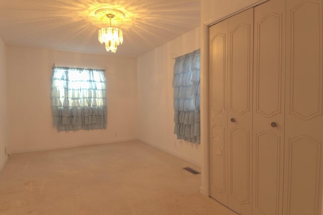 interior space featuring an inviting chandelier, visible vents, baseboards, and light carpet