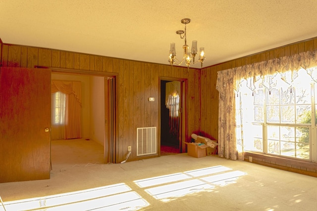 unfurnished dining area with a chandelier, visible vents, wood walls, and a wealth of natural light