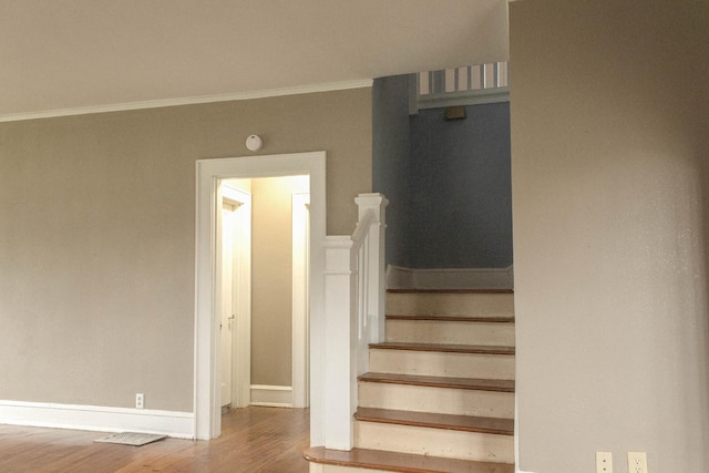 staircase with crown molding, wood finished floors, and baseboards