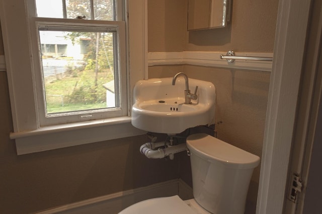 half bathroom with toilet, a textured wall, and a sink