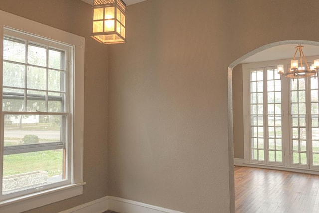 spare room with baseboards, arched walkways, an inviting chandelier, and wood finished floors