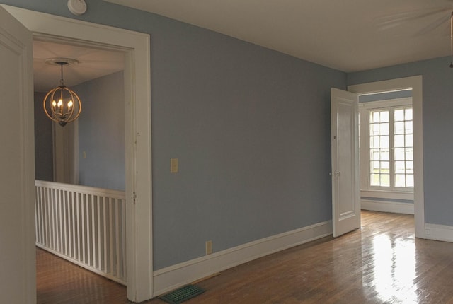 empty room with visible vents, wood finished floors, baseboards, and a chandelier