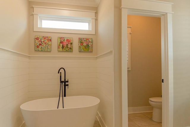 full bathroom featuring a soaking tub, toilet, tile patterned floors, and wainscoting