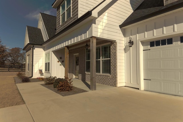 view of home's exterior with a garage, brick siding, board and batten siding, and a shingled roof