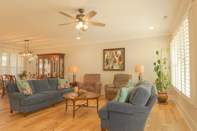 living room with visible vents, light wood-style floors, crown molding, baseboards, and ceiling fan