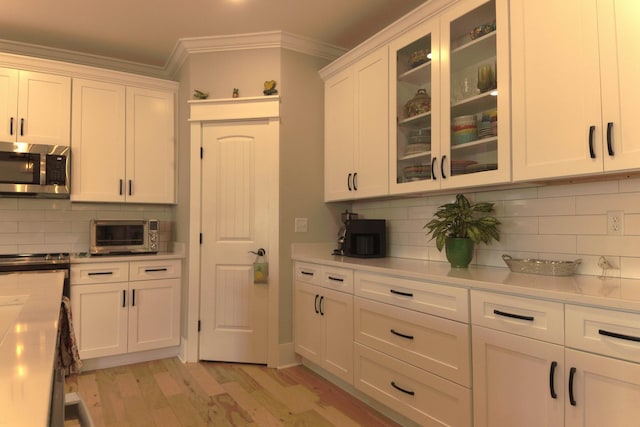 kitchen featuring white cabinetry, stainless steel microwave, light wood-style flooring, and ornamental molding