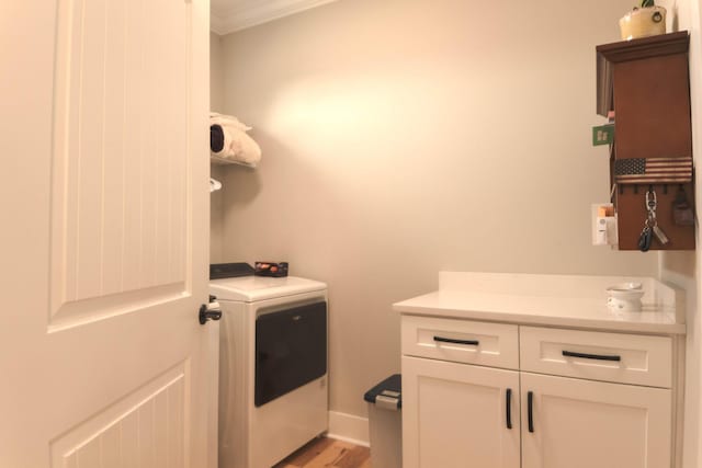 laundry room with baseboards, ornamental molding, washer / dryer, light wood-style flooring, and cabinet space