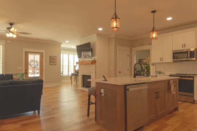 kitchen featuring a sink, open floor plan, appliances with stainless steel finishes, a brick fireplace, and light wood-type flooring