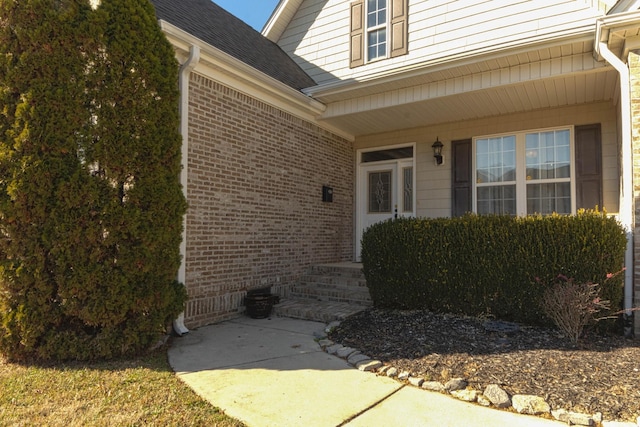 view of exterior entry with brick siding and roof with shingles