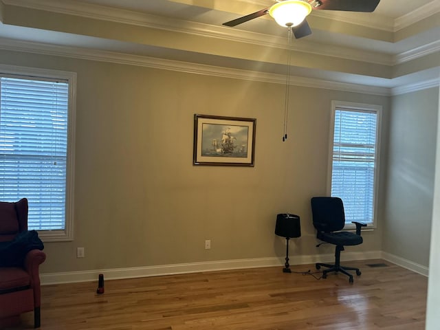 living area with a healthy amount of sunlight, a raised ceiling, ornamental molding, and wood finished floors