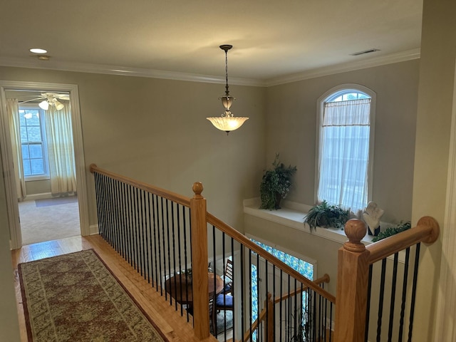 corridor featuring an upstairs landing, visible vents, a healthy amount of sunlight, and crown molding