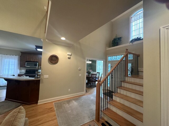 entrance foyer with stairs, crown molding, a healthy amount of sunlight, and light wood-type flooring