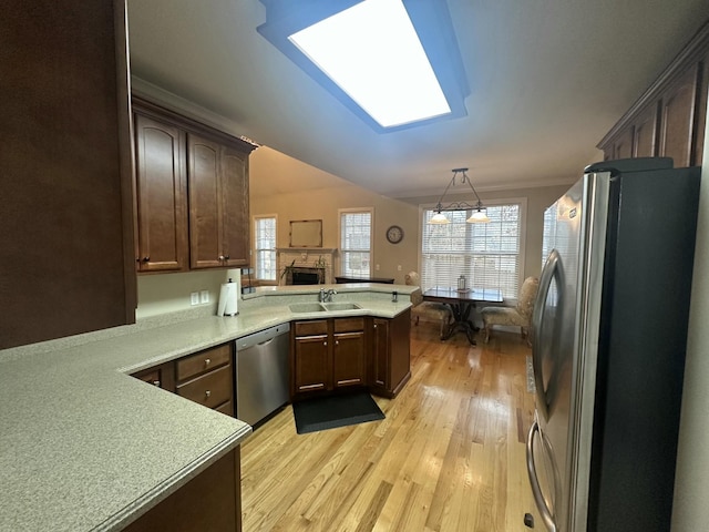 kitchen featuring a sink, stainless steel appliances, a peninsula, a skylight, and light countertops