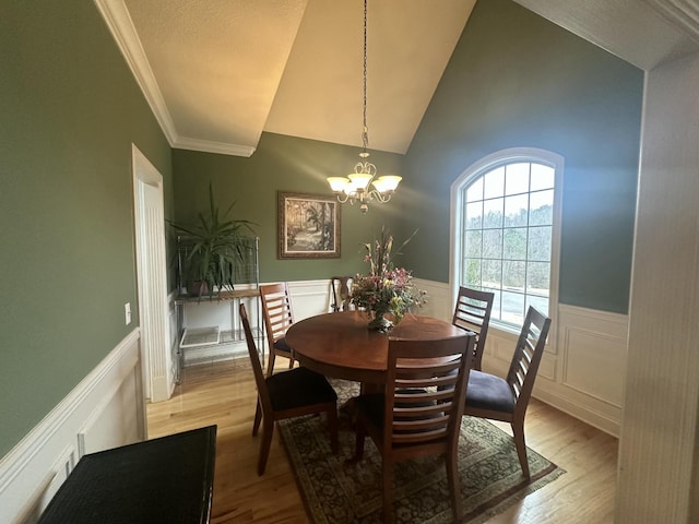 dining room with high vaulted ceiling, ornamental molding, light wood-style floors, wainscoting, and a chandelier