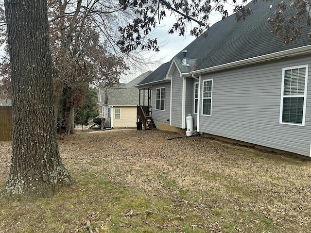 rear view of property featuring fence, a shingled roof, and entry steps