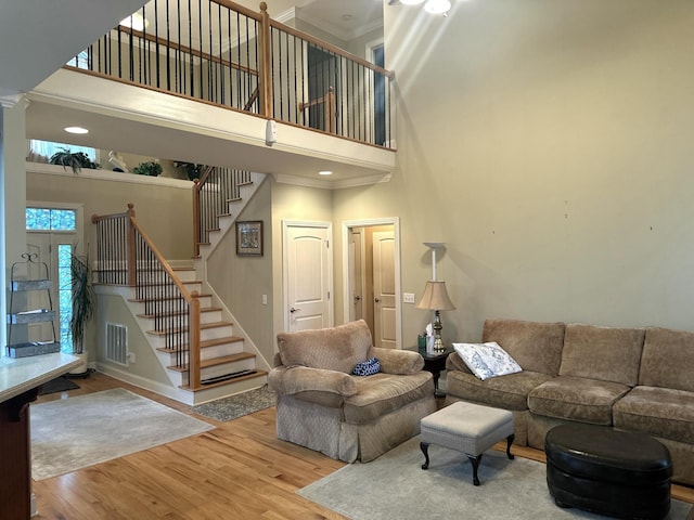 living room featuring stairway, wood finished floors, visible vents, a high ceiling, and crown molding