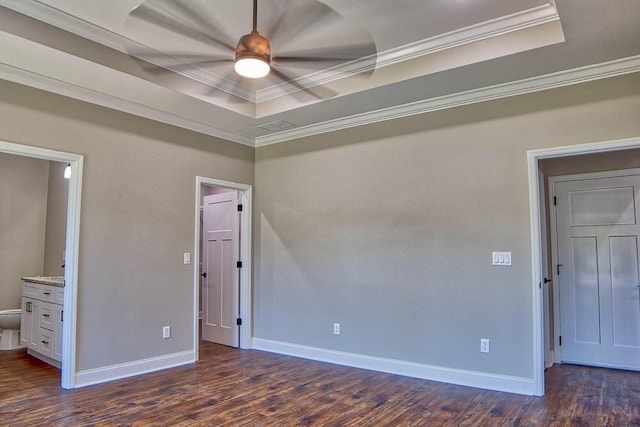 interior space with baseboards, dark wood finished floors, a tray ceiling, ensuite bath, and ornamental molding