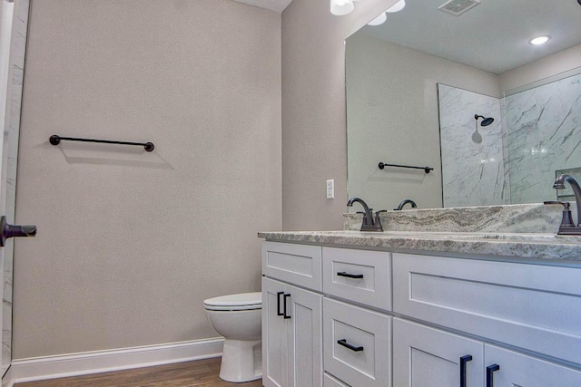 bathroom with toilet, wood finished floors, a marble finish shower, baseboards, and vanity