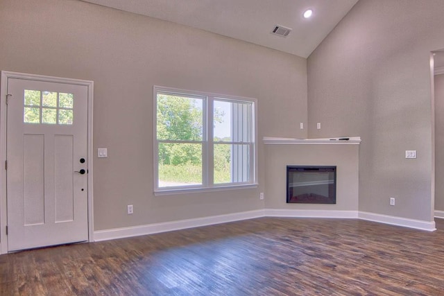 unfurnished living room with visible vents, dark wood-type flooring, a glass covered fireplace, baseboards, and vaulted ceiling