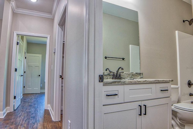 bathroom featuring baseboards, toilet, ornamental molding, wood finished floors, and vanity