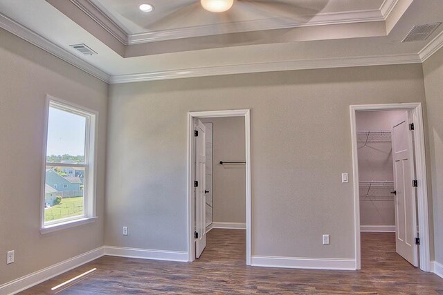 unfurnished bedroom featuring a walk in closet, visible vents, ornamental molding, a tray ceiling, and dark wood-style floors