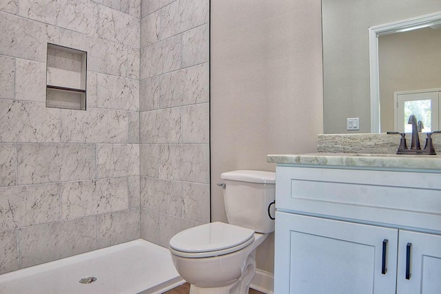 full bathroom featuring a tile shower, toilet, and vanity