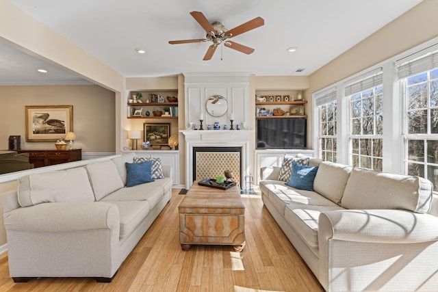 living room featuring a ceiling fan, light wood-style flooring, recessed lighting, a fireplace, and ornamental molding