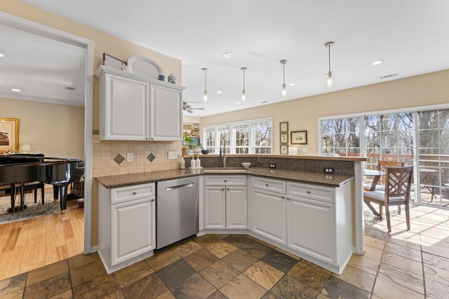 kitchen with stone tile floors, a sink, a peninsula, and stainless steel dishwasher