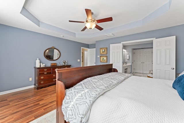 bedroom featuring a ceiling fan, wood finished floors, visible vents, baseboards, and a tray ceiling