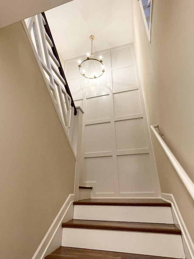 stairs with a decorative wall, a notable chandelier, and baseboards