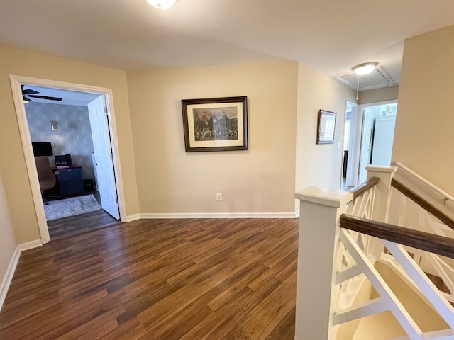 corridor featuring attic access, an upstairs landing, dark wood-type flooring, and baseboards