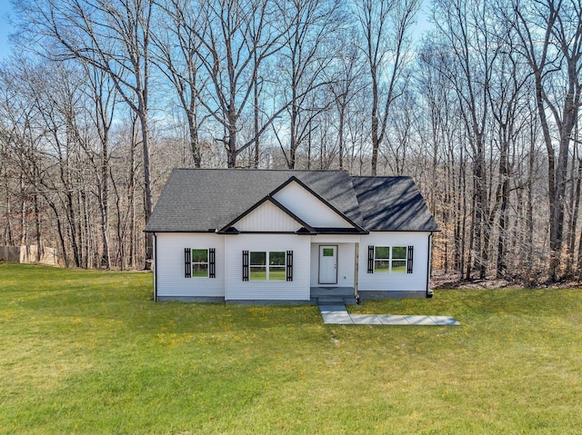 modern farmhouse with a view of trees, a front yard, and a shingled roof