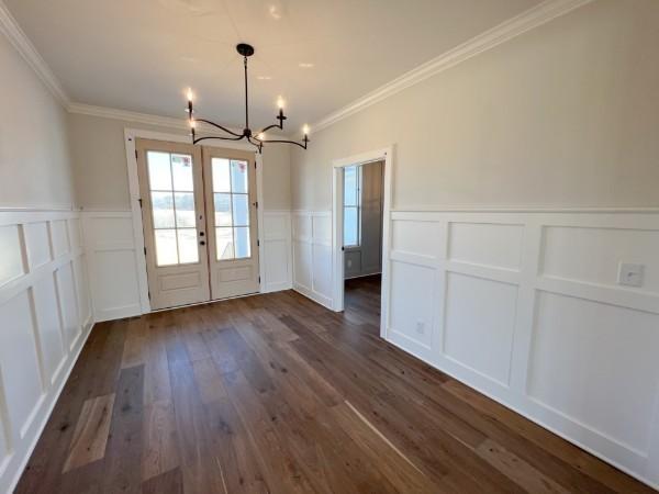 unfurnished dining area featuring a wainscoted wall, ornamental molding, french doors, an inviting chandelier, and dark wood-style flooring