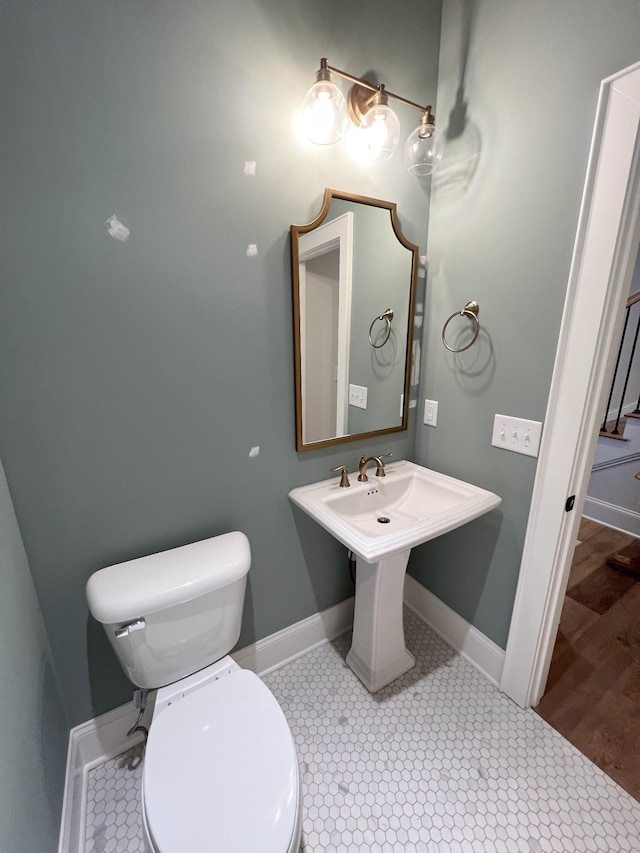 half bathroom featuring a sink, baseboards, toilet, and tile patterned flooring