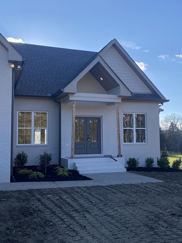 view of exterior entry featuring french doors, brick siding, and a shingled roof