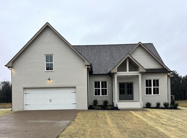 view of front facade with a shingled roof, a front yard, french doors, driveway, and an attached garage