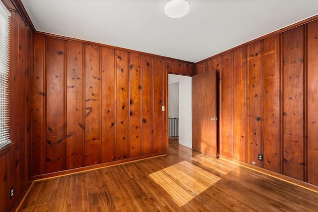 empty room with hardwood / wood-style flooring, baseboards, and wood walls